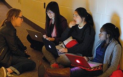 Four women sitting in a hallway with laptops